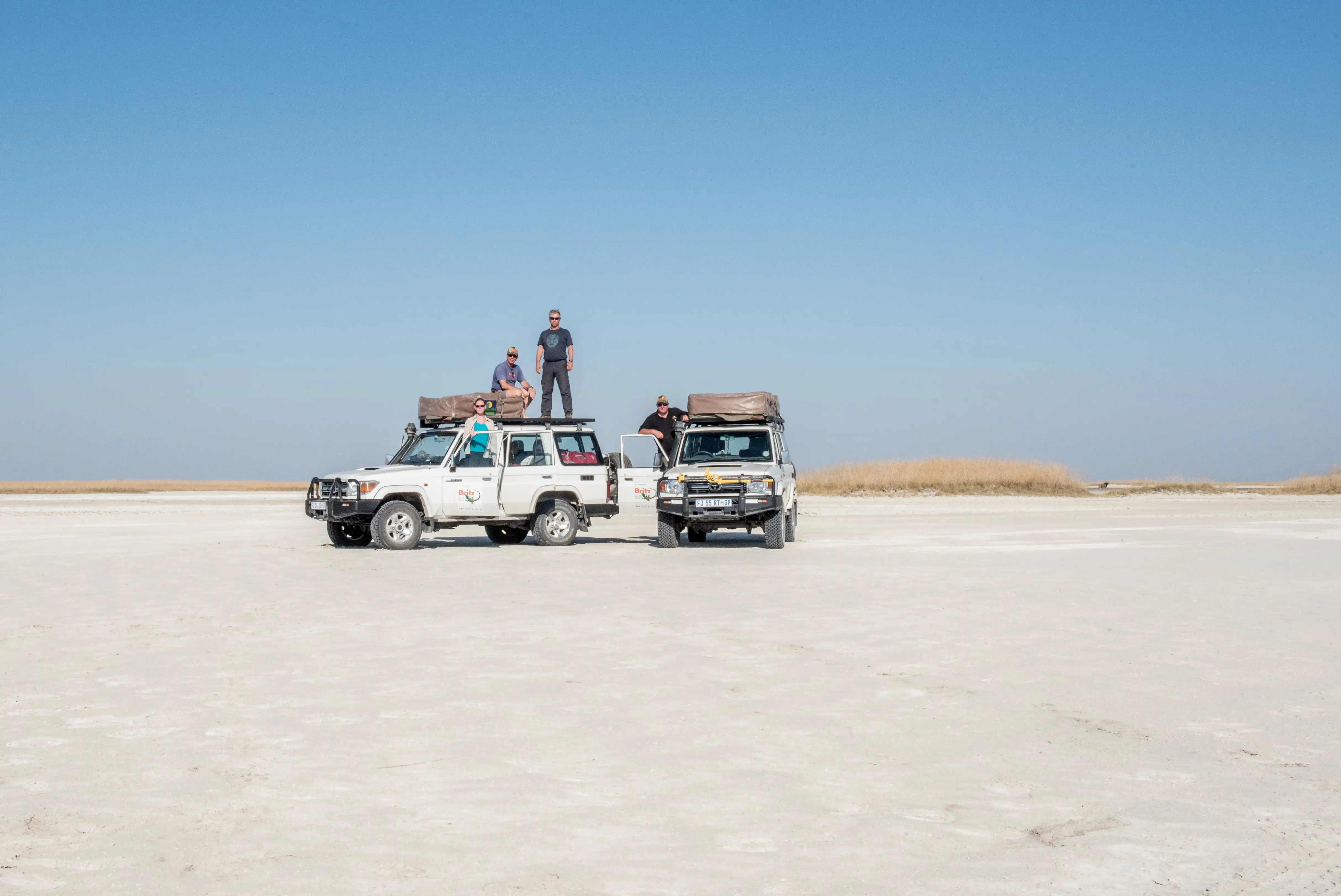 Two 4x4 campers in the desert in Botswana with people standing on the roof